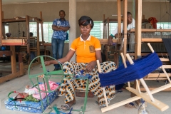 Woman weaving thread with her baby next to her