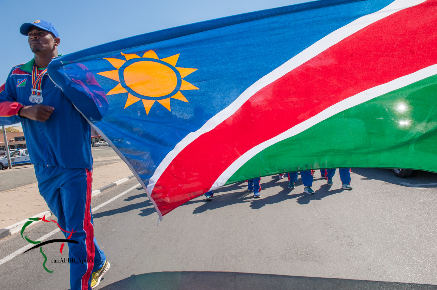 Male athlete leading a parade while holding Namibia flag.