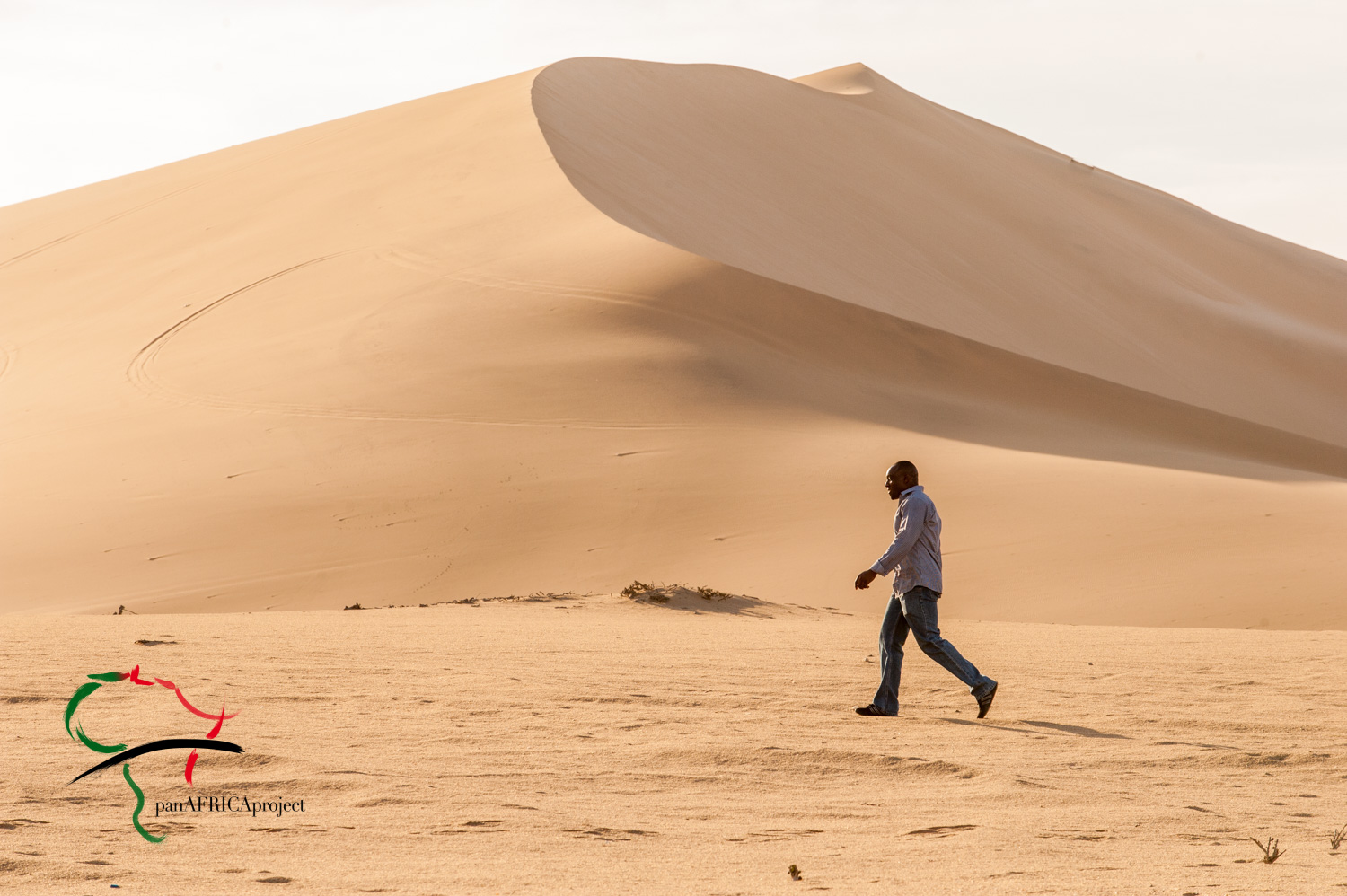 Man walking in front of sand dunes.