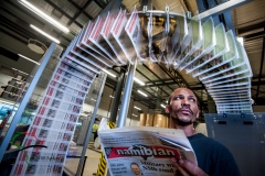 Newspapers running through a printing press while a worker reads one.